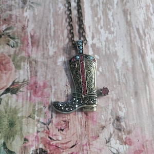 May include: A gold-tone necklace with a boot-shaped pendant. The boot is decorated with red and blue rhinestones and has a spur on the back.