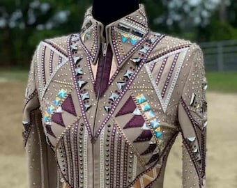 Op de afbeelding: Een beige showjas met een geometrisch ontwerp met paarse, witte en gouden accenten. De jas is versierd met strass en heeft een ritssluiting. De tekst "SARA FASHION STORE" is zichtbaar op de jas.