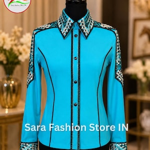 May include: A bright turquoise long-sleeve button-down shirt featuring black piping along the seams and a central placket. The collar, shoulders, and cuffs are heavily embellished with silver and black geometric crystal patterns. Sara Fashion Store IN.