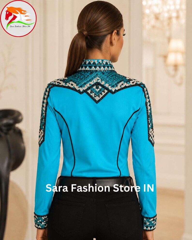 May include: A bright turquoise long-sleeve shirt featuring intricate black and silver geometric crystal embellishments across the shoulders, collar, and cuffs. The shirt includes black piping accents and is paired with black pants and a black belt.