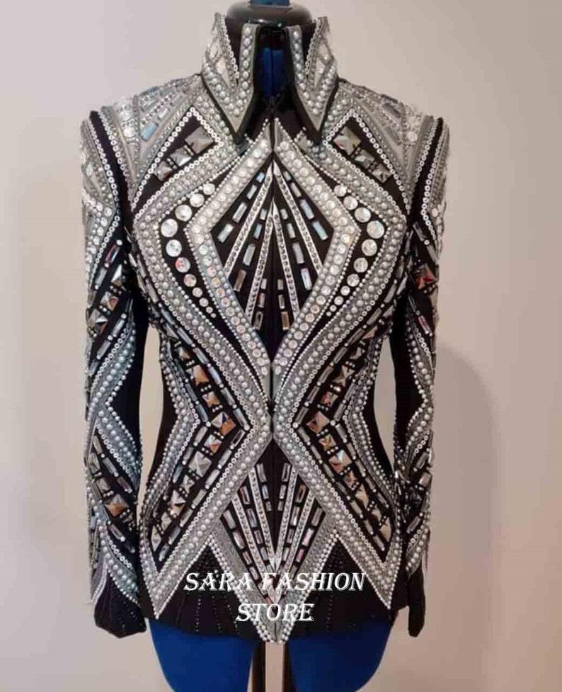 Op de afbeelding: Een zwart en zilveren showjasje met een ritssluiting en een geometrisch ontwerp. Het jasje is versierd met strass en parels. De tekst "SARA FASHION STORE" is gedrukt op de onderkant van het jasje.