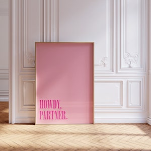Peut inclure: Une affiche encadrée rose avec le texte "Howdy, Partner." en lettres blanches.