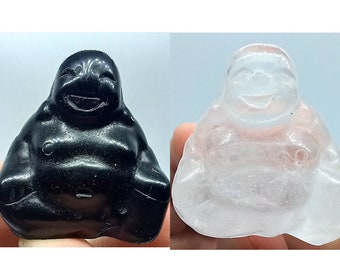 May include: Two laughing Buddha statues, one black and one white, carved from polished stone. The statues are sitting with their legs crossed and their hands resting on their bellies.