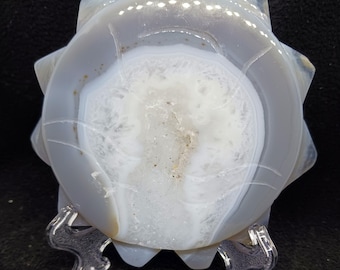 Op de afbeelding: Een witte en lichtblauwe agaat geode-plak met een stervorm. De geode staat op een transparante plastic standaard.