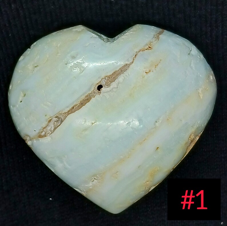 May include: A heart-shaped stone with a light blue and white striped pattern. A brown fissure runs across the stone. The number "1" is in red in the bottom right corner. The stone is likely a decorative item.