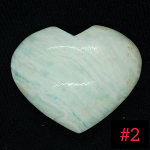 May include: A heart-shaped stone with a pale blue and white marbled pattern. The stone has a smooth, polished surface and a slight sheen. The number "#2" is in the bottom right corner.