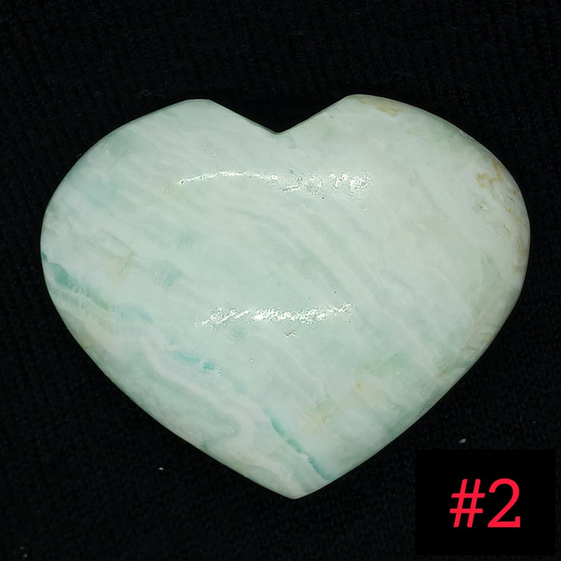 May include: A heart-shaped stone with a pale blue and white marbled pattern. The stone has a smooth, polished surface and a slight sheen. The number "#2" is in the bottom right corner.