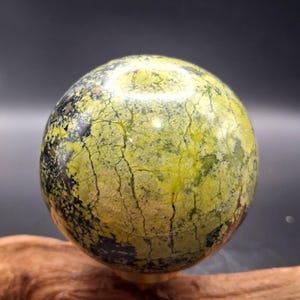 May include: A polished spherical stone featuring a vibrant lime green and chartreuse base color with intricate dark brown and black veining throughout the surface. The sphere displays a smooth, glossy texture with natural mineral inclusions.