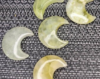 May include: Five green and yellow crescent moon shaped polished stones. The stones are arranged in a semi-circle on a grey textured surface.