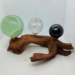May include: Three crystal spheres, one green, one clear, and one black, are displayed on a wooden branch. The spheres are mounted on metal stands.