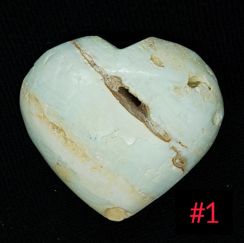 May include: A heart-shaped stone in shades of pale blue and beige. The stone features a crack and a hole. The number "#1" is displayed in red in the bottom right corner.