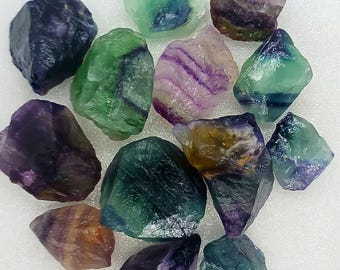 May include: A collection of 12 fluorite crystals in various shades of green, purple, and blue. The crystals are rough and have a natural, unpolished look.