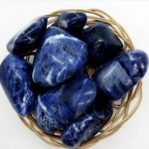 May include: A collection of smooth, polished blue and white sodalite tumbled stones in a woven basket. The stones have a variety of patterns and shades of blue.