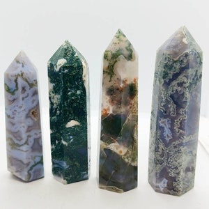 May include: Four moss agate crystal points with different patterns of green, white, and purple. The points are all about the same size and are arranged in a row.