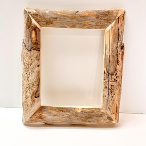 May include: A rustic, square picture frame made from natural wood. The frame has a rough, textured surface with visible knots and grain, showcasing a light brown color. The frame is designed to hold a photograph or artwork.