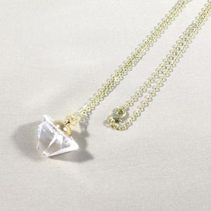 May include: A gold chain necklace with a clear crystal pendant shaped like a perfume bottle.