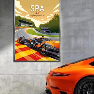 Puede incluir: Un p&oacute;ster enmarcado con un coche de carreras de F&oacute;rmula 1 en una pista, con el texto "SPA Belgium Grand Prix". El coche es naranja y negro, y el p&oacute;ster tiene un estilo vintage. Un coche deportivo naranja est&aacute; aparcado junto al p&oacute;ster.