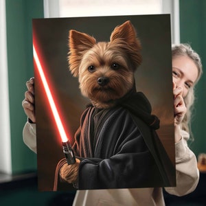 May include: A canvas print featuring a Yorkshire Terrier dressed as a Jedi, holding a red lightsaber. The dog is wearing a black hooded robe against a dark background. The artwork is held by a person.