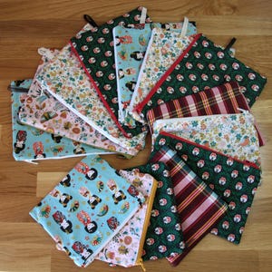 Peut inclure: Une collection de pochettes zippées rectangulaires en tissu disposées en éventail. Les pochettes présentent divers motifs, notamment des poupées japonaises stylisées, des imprimés floraux, des carreaux et des motifs vert foncé.