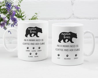 May include: Two white ceramic mugs with black bear silhouettes and the text "mama bear". The text "All a mama need is coffee and her cubs" is printed below the bear. Each mug has a different set of names printed below the text.