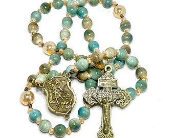 May include: A green and brown rosary with a bronze cross and a bronze medal of Saint Michael the Archangel. The medal features the text "Sanctus Michael Archangelus" and "Ora Pro Nobis".