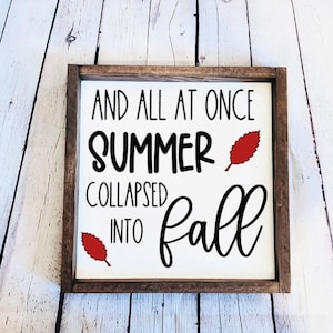 May include: A wooden sign with the text "And all at once summer collapsed into fall" in black lettering. The sign has two red leaf accents.