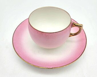 May include: A pink teacup and saucer set with a gold rim. The cup and saucer have a gradient design, fading from white to pink.