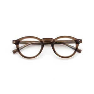 May include: Round eyeglasses with a translucent brown acetate frame. The glasses feature a keyhole bridge, clear lenses, and silver-toned metal rivets on the front corners of the frame. The inner temple arm displays gold-colored text markings.