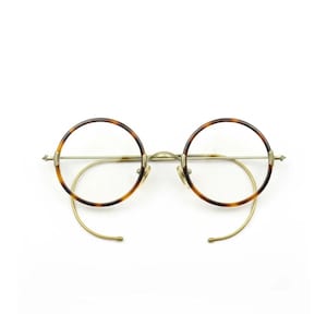 May include: Round spectacles featuring thin, metallic gold-toned frames and a tortoiseshell pattern on the circular rims. The glasses include curved, wire-style temple arms that loop behind the ears and adjustable nose pads on a central bridge.