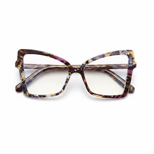 Puede incluir: Gafas de estilo ojo de gato de gran tamaño con un patrón de carey multicolor con motas de color púrpura, azul, amarillo y marrón. La montura tiene una forma angular distintiva con lentes transparentes y patillas finas a juego visibles.