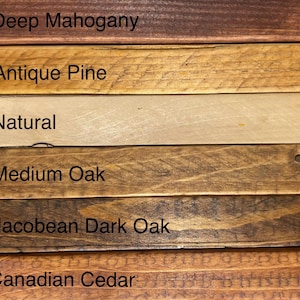 May include: Close-up of six wooden planks with different stain colors. The colors include Deep Mahogany, Antique Pine, Natural, Medium Oak, Jacobean Dark Oak, and Canadian Cedar. Each plank has the color name printed on it.