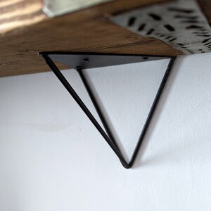 May include: Black metal shelf bracket with a triangular design. The bracket is attached to a wooden shelf.