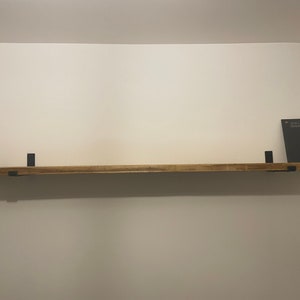May include: A wooden shelf with black metal brackets. The shelf is mounted on a white wall. A small black chalkboard with the text "Just Love Remember It" is sitting on the shelf.