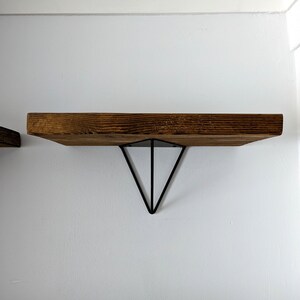 May include: A wooden shelf with a triangular metal bracket. The shelf is brown and the bracket is black.
