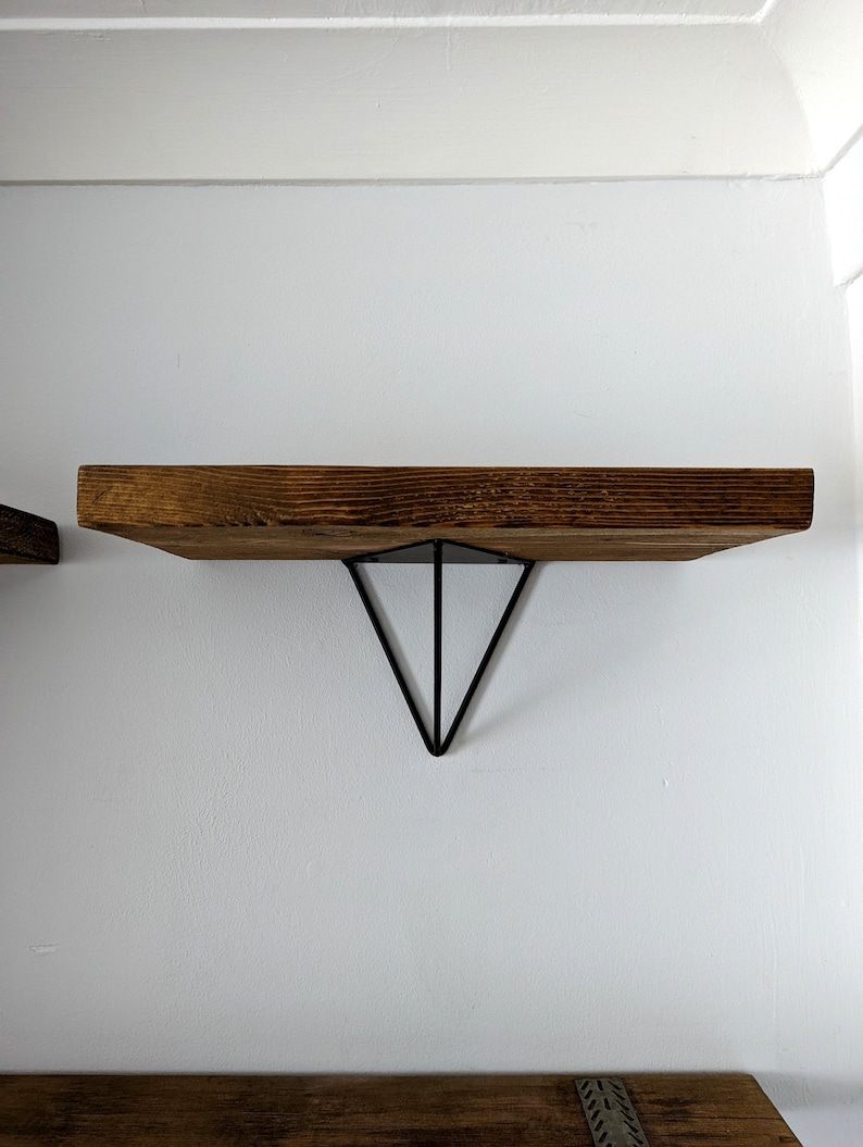 May include: A wooden shelf with a triangular metal bracket. The shelf is brown and the bracket is black.