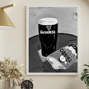 Peut inclure: Impression en noir et blanc d'une pinte de Guinness avec le logo Guinness et un paquet de chips Tayto au fromage et &agrave; l'oignon. L'&oelig;uvre est encadr&eacute;e en blanc.