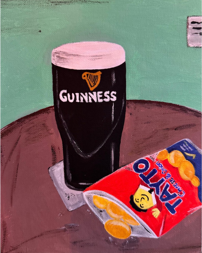 Peut inclure: Peinture d'une pinte de Guinness avec une t&ecirc;te cr&eacute;meuse, le logo Guinness est visible. &Agrave; c&ocirc;t&eacute; de la pinte, un sachet de chips Tayto Cheese & Onion partiellement ouvert. Le fond est vert.