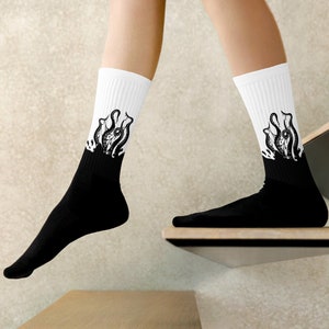 May include: A pair of white socks with black ink illustrations of an octopus on the top of each sock. The socks are pulled up to the calf and the bottom of the socks are black.