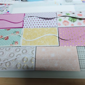 May include: Eight different patterned card envelopes with a wavy flap design. The envelopes are arranged in two rows of four. The patterns include floral, polka dot, hearts, and geometric designs.