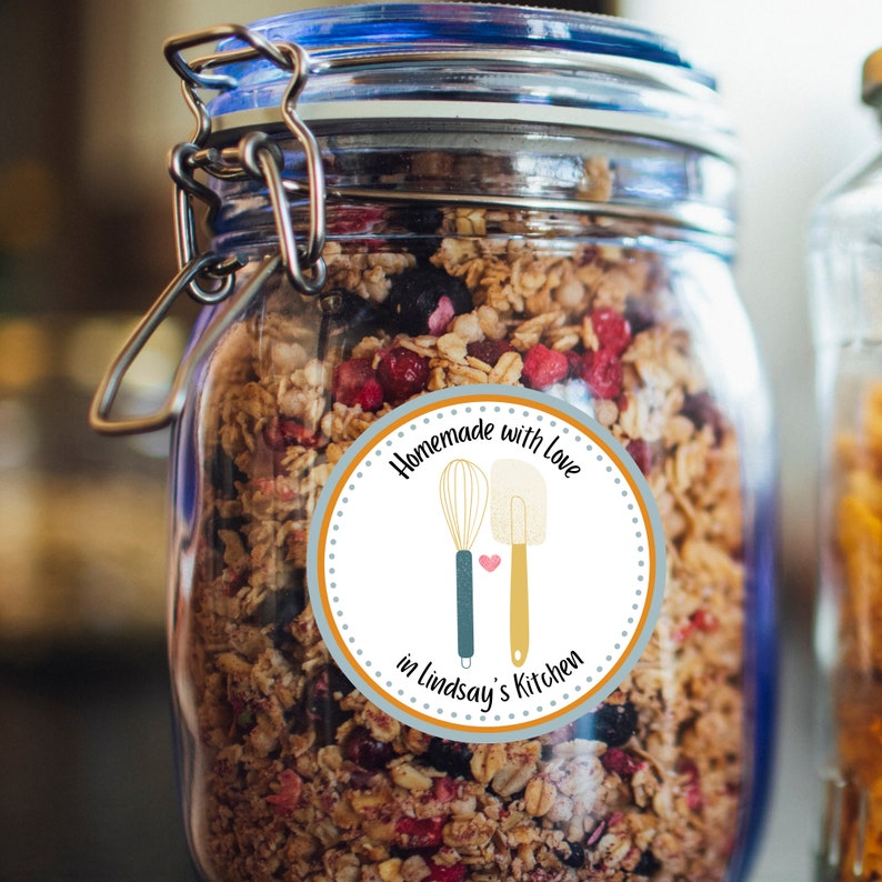 May include: A glass jar filled with granola with dried fruit and nuts. A round sticker on the jar reads "Homemade with Love in Lindsay's Kitchen" with a whisk and spatula illustration.