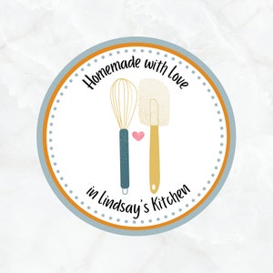 May include: A blue and orange circle with white polka dots and the text "Homemade with love in Lindsay's Kitchen". Inside the circle are illustrations of a whisk and a spatula with a pink heart between them.