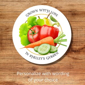 Op de afbeelding: Ronde witte sticker met een gouden cirkelrand. De sticker heeft een afbeelding van verse groenten en fruit, waaronder een tomaat, paprika, wortel, komkommer, peer en groene bladeren. De tekst op de sticker luidt "Grown with Love in Shelley's Garden".