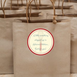 May include: Brown paper gift bags with a red and white circle sticker that says "A little something whipped up in Adriana's kitchen... Just for you!" with a red whisk illustration.