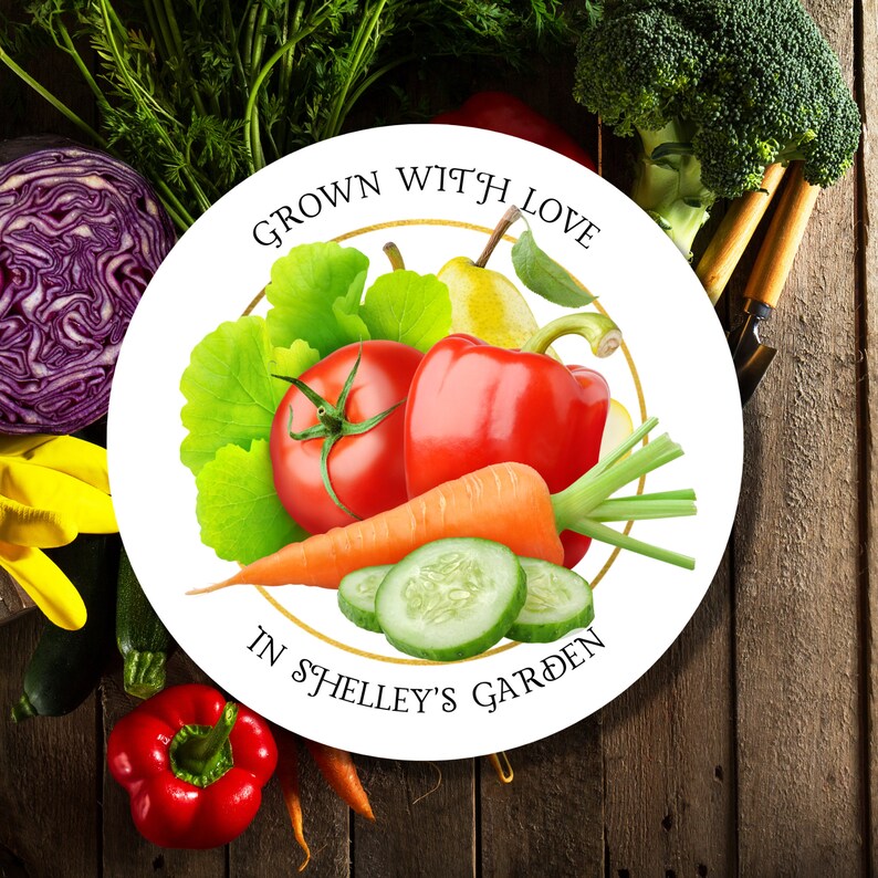 Op de afbeelding: Ronde witte sticker met een gouden cirkel rond de rand. De sticker zegt "Grown with Love in Shelley's Garden". Binnen de cirkel bevinden zich illustraties van een tomaat, een rode paprika, een wortel, een komkommer, een peer en sla.