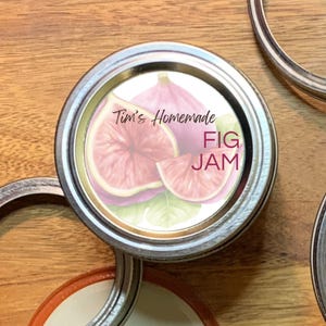 Peut inclure: Un couvercle de pot en argent avec une étiquette blanche qui dit "Tim's Homemade Fig Jam". L'étiquette présente une illustration aquarelle de figues.