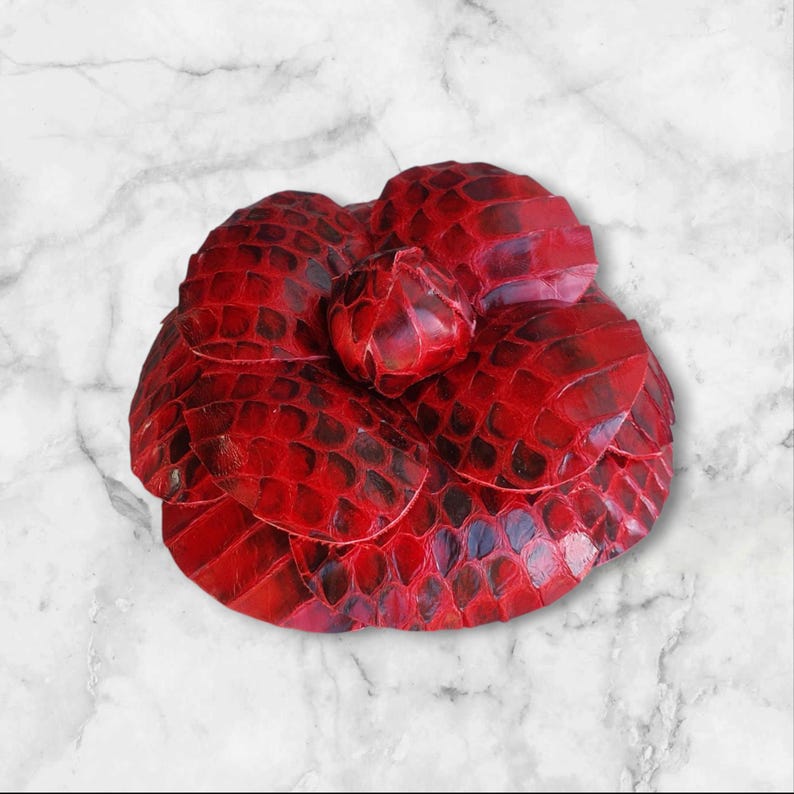 May include: A red leather flower brooch with a textured, scaly surface.