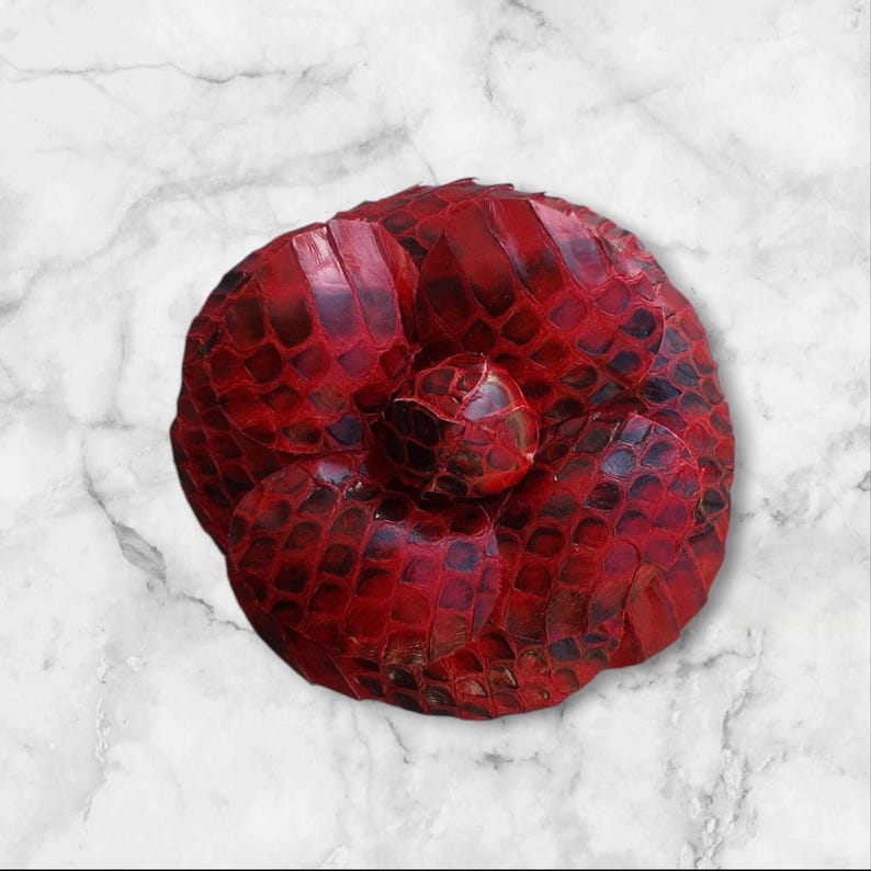 May include: A red leather flower brooch with a textured snake skin pattern.
