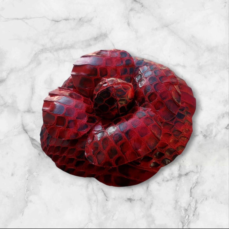 May include: A red leather flower brooch with a textured, snake-skin like pattern.