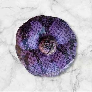 Könnte beinhalten: Eine violette und schwarze Brosche in Blumenform mit Schlangenhautmuster.