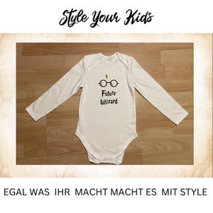 Könnte beinhalten: Weißer Baby-Body mit langen Ärmeln und dem Text "Future Wizard" in Schwarz, zusammen mit einem Blitz- und Brillen-Motiv. Oben im Bild steht "Style Your Kids". Unten im Bild steht "EGAL WAS IHR MACHT MACHT ES MIT STYLE".